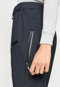 Παντελόνι εξωτερικού χώρου σε ναυτικό μπλε με κομψό σχέδιο, που διαθέτει πλαϊνή τσέπη με φερμουάρ, ρυθμιζόμενη ζώνη και απαλό υλικό για άνεση.