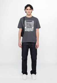 Gray cotton T-shirt with graphic text "REMEMBER BOREDOM?" and illustration, paired with dark blue jeans and white sneakers.