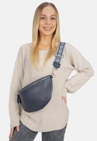 Navyfarbene Leder-Crossbody-Tasche mit abgerundeter Form, silbernem Reißverschluss und gemustertem Stofftragegurt in Blau- und Weißtönen. Strukturierte Oberfläche.