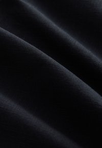 Tissu noir foncé avec une texture tissée subtile et des plis doux créant des ombres et des reflets délicats.