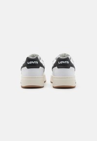 Hvite skinn sneakers med svart hælaccent som har Levi's-logo, tykk kremfarget såle og en jevn tekstur.