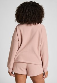Roze fleece sweatshirt met verlaagde schouders, gecombineerd met bijpassende shorts. Zachte textuur, losse pasvorm en minimale naaddetails.