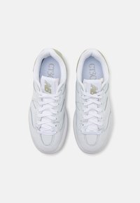 Des chaussures de sport en cuir blanc présentent une texture lisse, un bout rond, des lacets plats et des accents gris subtils. Logo visible sur la languette.