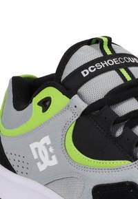 Baskets DC grises et noires avec des accents vert néon, en tissu maille, avec logo sur le côté et la sangle de la languette.