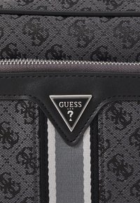 Bolso de mano de tela en negro y gris con un patrón texturizado de logo. Presenta un cierre de plata, una etiqueta con el logo en forma de triángulo y acentos de rayas verticales.
