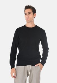 Maglione nero a coste con maniche lunghe e scollo rotondo. Abbinato a pantaloni grigi chiari. Tessuto liscio con un look aderente.