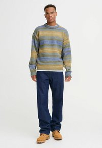 Gestreifter Pullover aus Strick in Blau und Beige, runder Halsausschnitt, lässige Passform. Kombiniert mit dunkelblauen Hosen und braunen Schuhen.