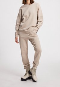 Felpa beige con maniche lunghe e polsini a coste, abbinata a pantaloni jogger coordinati. Calzature: stivali chiari con lacci e suola spessa.