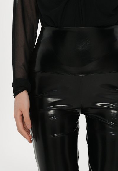 Sorte højtaljede leggings lavet af glat, strækbart materiale. Har en glat tekstur med subtile folder langs benene.