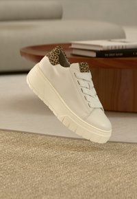 Baskets en cuir blanc avec un accent imprimé léopard au talon, dotées d'une semelle épaisse et de lacets croisés. Détail de surface texturée visible.