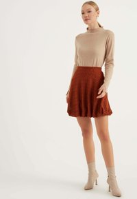 Beige stickad topp med långa ärmar, tillsammans med en rostfärgad utsvängd kjol med ett zickzackmönster, och beige ankelboots.