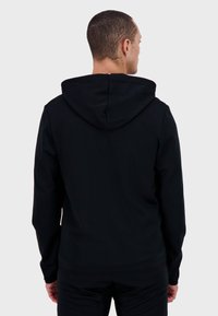 Felpa nera con grande stampa sul retro, polsini a costine e cappuccio regolabile con lacci. Realizzata in tessuto morbido con una texture liscia.