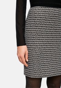 Black and white patterned skirt featuring an uneven dotted design, made from textured fabric, worn with a fitted black long-sleeve top.