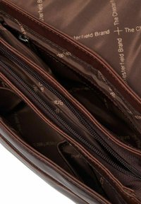 Interno di una borsa in pelle marrone con diversi scomparti con cerniera e una fodera liscia stampata con "The Chesterfield Brand."