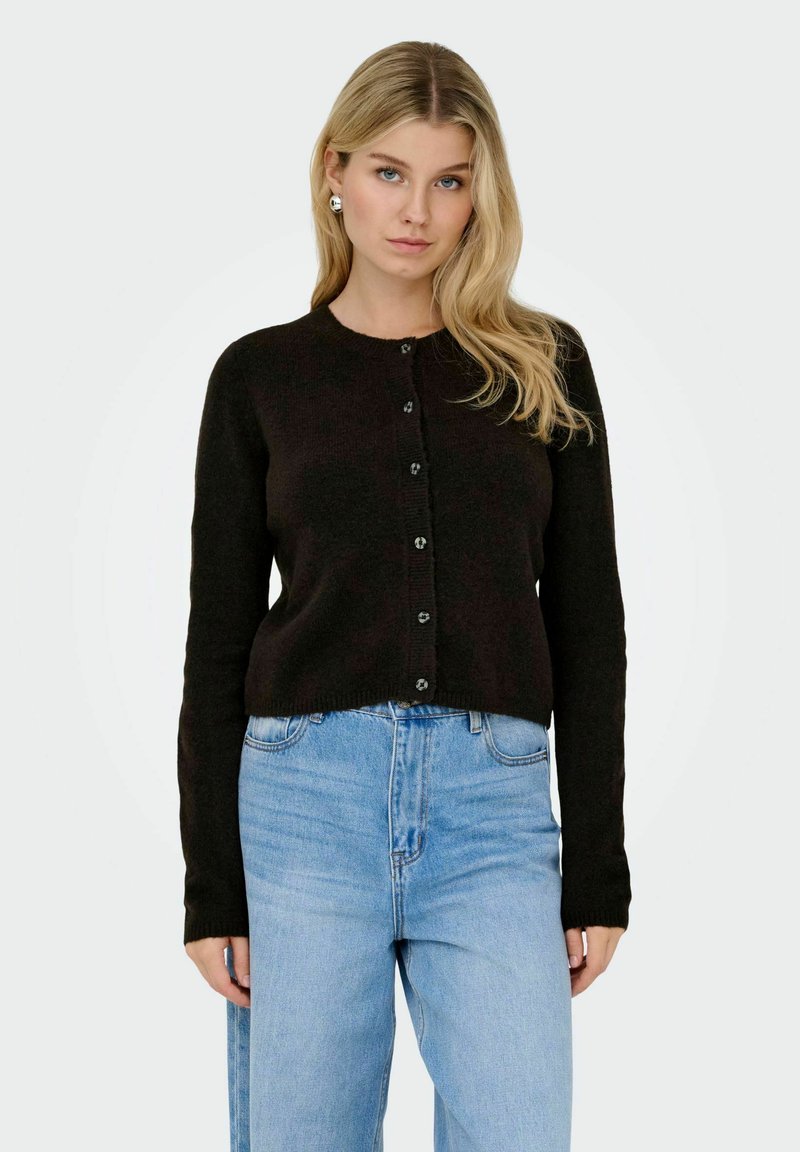 Cardigan nero lavorato a maglia con maniche lunghe, scollo rotondo e chiusura con bottoni. Abbinato a jeans di denim a vita alta di colore blu chiaro.