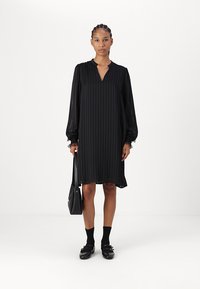 Črna dolga obleka s kratkimi rokavi in navpičnimi naborki, V-izrezom in napihnjenimi rokavi. Oblečena z črnimi nogavicami in čevlji, v kombinaciji s črno torbico.