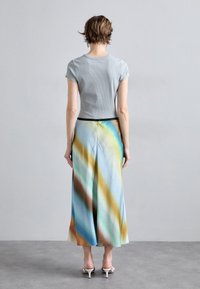 T-shirt à rayures gris clair et une longue jupe avec un motif diagonal multicolore dans des tons de bleu, vert et marron, avec une taille noire.