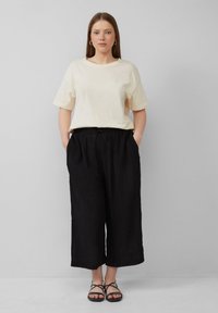 Crème katoenen T-shirt met korte mouwen, gecombineerd met losse, gestructureerde zwarte broek en zwarte sandaaltjes met banden.