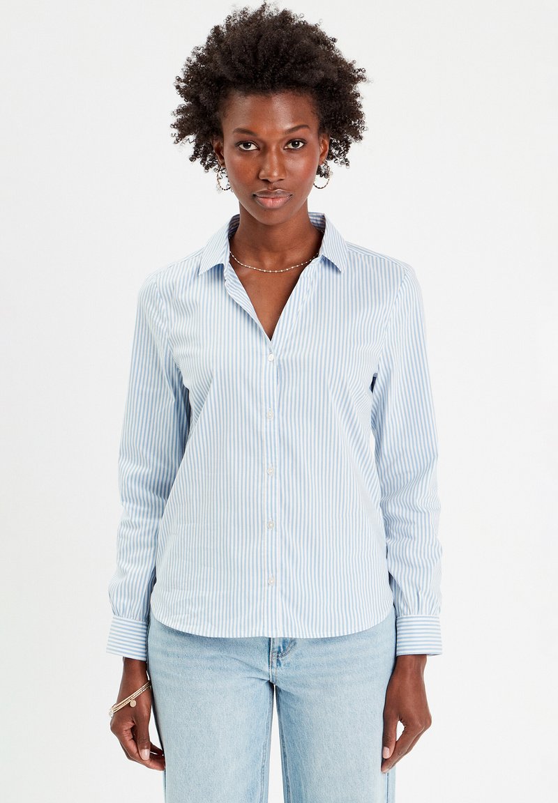 Chemise à boutons à rayures bleu clair et blanche, avec un col, des manches longues et une finition en tissu lisse. Présente une coupe normale et des boutons sur le devant.