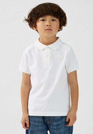 Witte katoenen polo shirt met een kraag, kort gerolde mouwen en een klein rond logo-patch. Draagt met blauwe spijkerjeans.