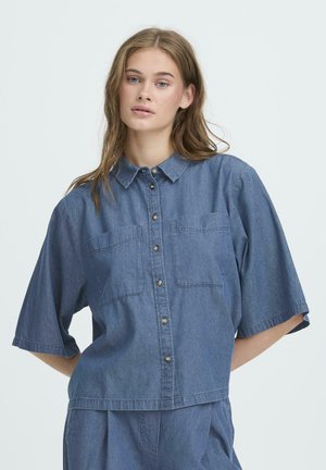 Denimhemd in mittlerem Blau, kurze Ärmel, zwei Brusttaschen, durchgehende Knopfleiste mit dunklen Knöpfen und lockerer Passform. Baumwollstoff.