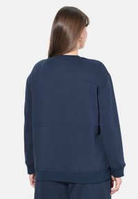 Felpa blu navy con una vestibilità rilassata, caratterizzata da polsini e orlo a coste, dettagli di cucitura visibili e finitura in tessuto testurizzato.