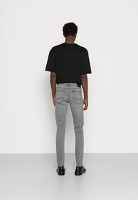 Svart t-shirt med korta ärmar kombinerad med smala grå jeans med fickor och svarta skor. Enkel design med en neutral färgpalett.