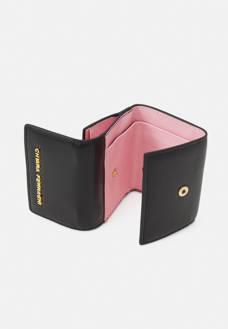 Portefeuille en cuir noir avec une texture lisse et des coutures blanches. L'intérieur présente une doublure rose et des ferrures dorées avec une fermeture à pression.