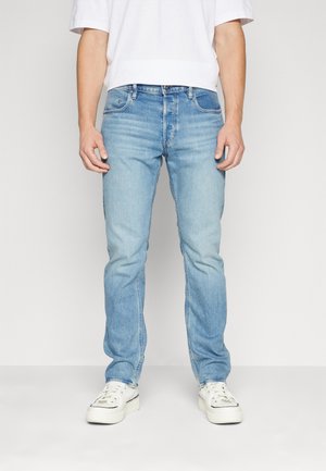 Jean en denim bleu clair avec une coupe droite, design à cinq poches, finition délavée et détails de couture subtils, portés avec des baskets blanches.