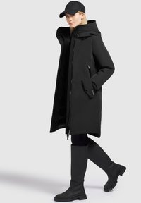 Czarny parka z kapturem, zamek błyskawiczny z przodu i bocznymi kieszeniami; połączona z czarnymi butami do kolan. Gładka tekstura, minimalistyczny design.