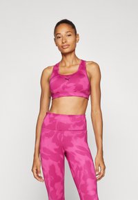 Sujetador deportivo rosa y leggings de cintura alta con un patrón de camuflaje. El material es elástico y de textura suave. Presenta el logo en el sujetador.