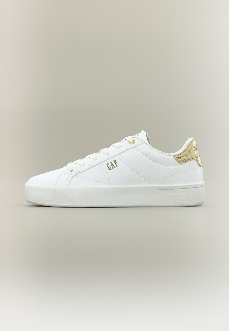 Baskets basses blanches avec accent doré au talon, lacets blancs, et logo "GAP" sur le côté, sur fond neutre uni.