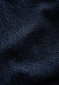 Tume indigo denimkangas, millel on sile tekstuur ja peen sära, diagonaalsed kudumismustrid ja väiksed värvi sügavuse variatsioonid.