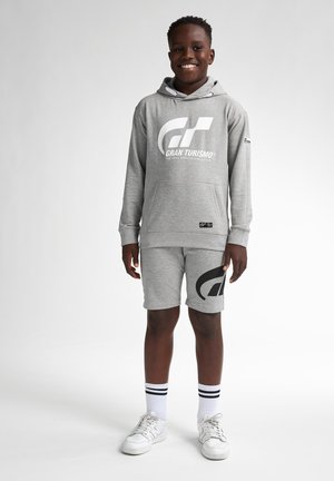 Felpa grigia con logo bianco "Gran Turismo", abbinata a pantaloni corti coordinati con un grande logo nero. Accentuata da calze a righe bianche e nere.