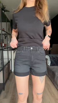 T-shirt preta combinada com calções de ganga escuros com bainhas dobradas, design de cinco bolsos e fecho com botão. Textura suave, ajuste casual.