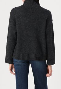 Personne portant un pull en tricot gris foncé avec ourlet et poignets côtelés, associé à un jean bleu foncé, vue de dos.