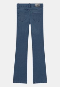 Flared blue jeans with a smooth texture, featuring two back pockets and a branded leather patch at the waistband.