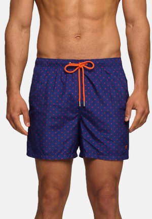 Torso maschile e parte superiore delle gambe con pantaloncini da bagno blu navy a pois rossi e coulisse arancione annodata davanti.