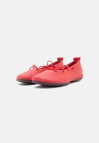 Red, flexible shoes with a smooth, textured finish, featuring a slip-on design and laces at the front. Low-profile rubber sole.
