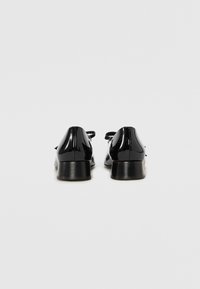 Black patent leather shoes with a low heel, featuring a smooth texture and a bow accent on the back. Clean design, no visible patterns.