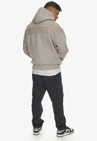 Sweat à capuche beige clair avec le texte "DROPSIZE" dans le dos, associé à un pantalon cargo noir et des baskets noir et blanc.