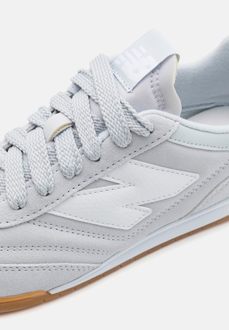 Chaussure de sport gris clair en suède et en matériaux synthétiques. Caractéristiques : lacets tissés, semelle en caoutchouc et un logo blanc contrastant.