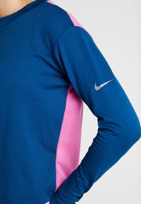Sportliches Langarmoberteil mit blauer Front, pinkem Seitenpaneel, strukturiertem Stoff und silbernem Nike-Logo auf dem linken Ärmel.