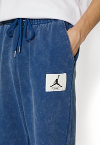 Blaue Baumwoll-Sweatpants mit einem Kordelzugbund, ausgestattet mit einem weißen Etikett mit einem schwarzen Silhouettenlogo und dem Text "Flight" auf der Tasche.