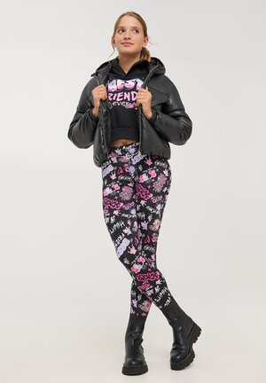 Giacca a vento nera con cappuccio, felpa nera corta con testo rosa "BEST FRIENDS" e leggings vivaci con motivi grafici colorati.