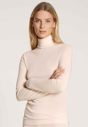 Light beige turtleneck top made from soft, stretchy fabric. It has long sleeves and a fitted silhouette, designed for a smooth, layered look.