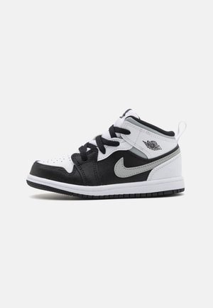 Basket montante noire, blanche et grise avec des lacets noirs, un logo Nike swoosh et un logo Air Jordan Wings sur le col de la cheville, vues de profil.
