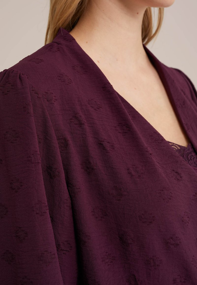 Levendige bordeaux blouse met delicate gegraveerde bloemenpatronen, lichtgewicht stof, diepe V-halslijn en brede, vallende mouwen.