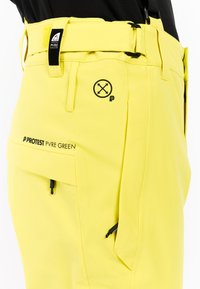 Gele buitensportbroek met verstelbare riem, zijzakken, zwarte hardware en het merkteken "PROTEST" langs de onderkant van het been. Gladde stoftextuur.