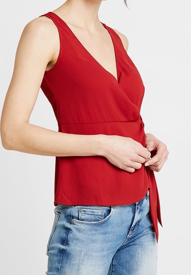 Haut sans manches rouge avec un décolleté en V profond et un design enveloppant. Fabriqué en tissu lisse, il présente un accent noué à la taille et une coupe décontractée.